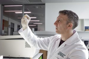 Research scientist in a white lab coat examining a Calocurb capsule in a laboratory.