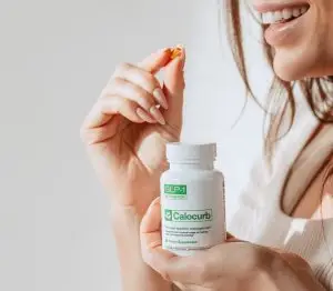 Smiling woman holding a Calocurb supplement bottle in one hand and a capsule in the other.