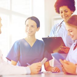 Healthcare team meeting in a medical office, with doctors and nurses reviewing patient information on tablets and a clipboard, representing practice growth, digital health solutions, and provider collaboration.